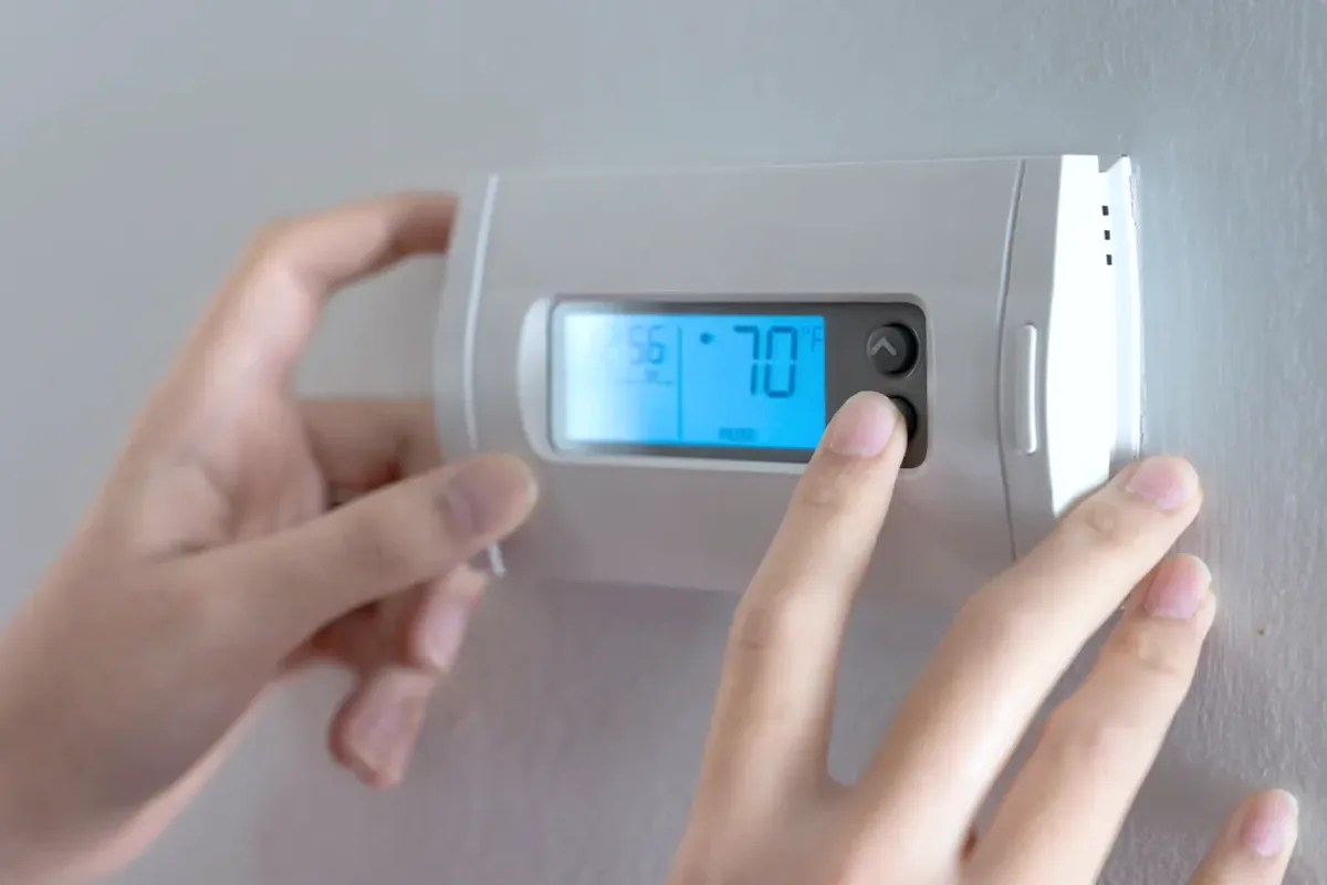 Hands adjusting a digital wall thermostat