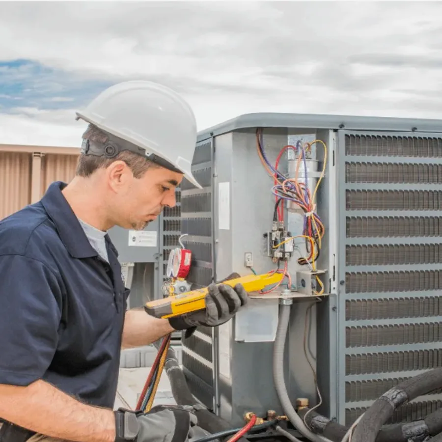 HVAC technician in a hard hat testing an outdoor air conditioner with a multimeter